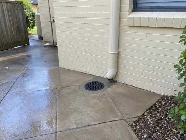 Clean outdoor drain grate in paved side yard beside a brick house in Berowra