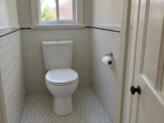Clean white toilet in a tiled small bathroom with window and toilet paper holder in Asquith