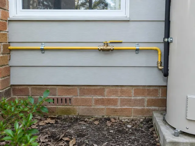 Yellow gas pipe with valve on exterior house wall beside brickwork and a hot water unit in Mount Colah
